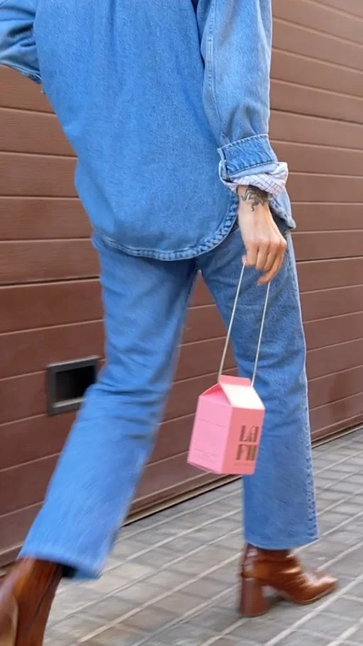 Woman in denim walking with a pink La Fille Milk Box in hand.