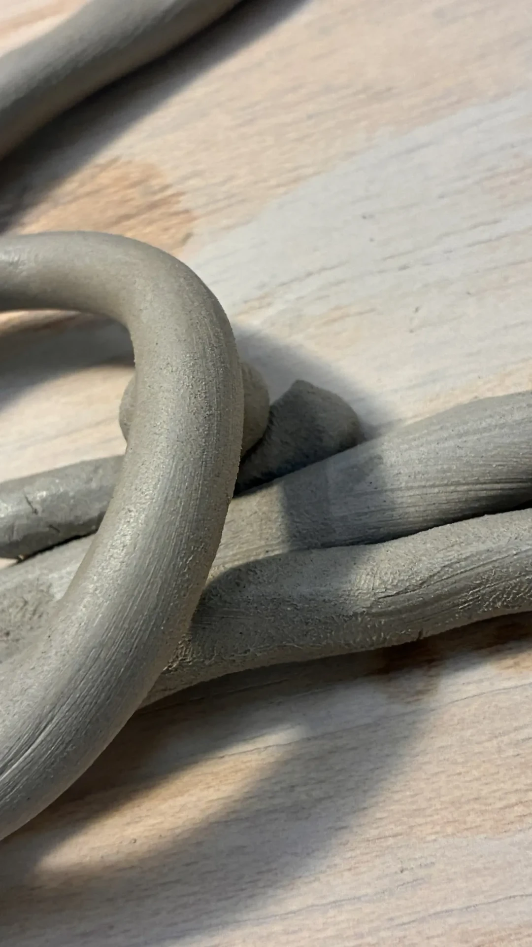 Loops of raw grey clay resting on a sunlit wooden surface.