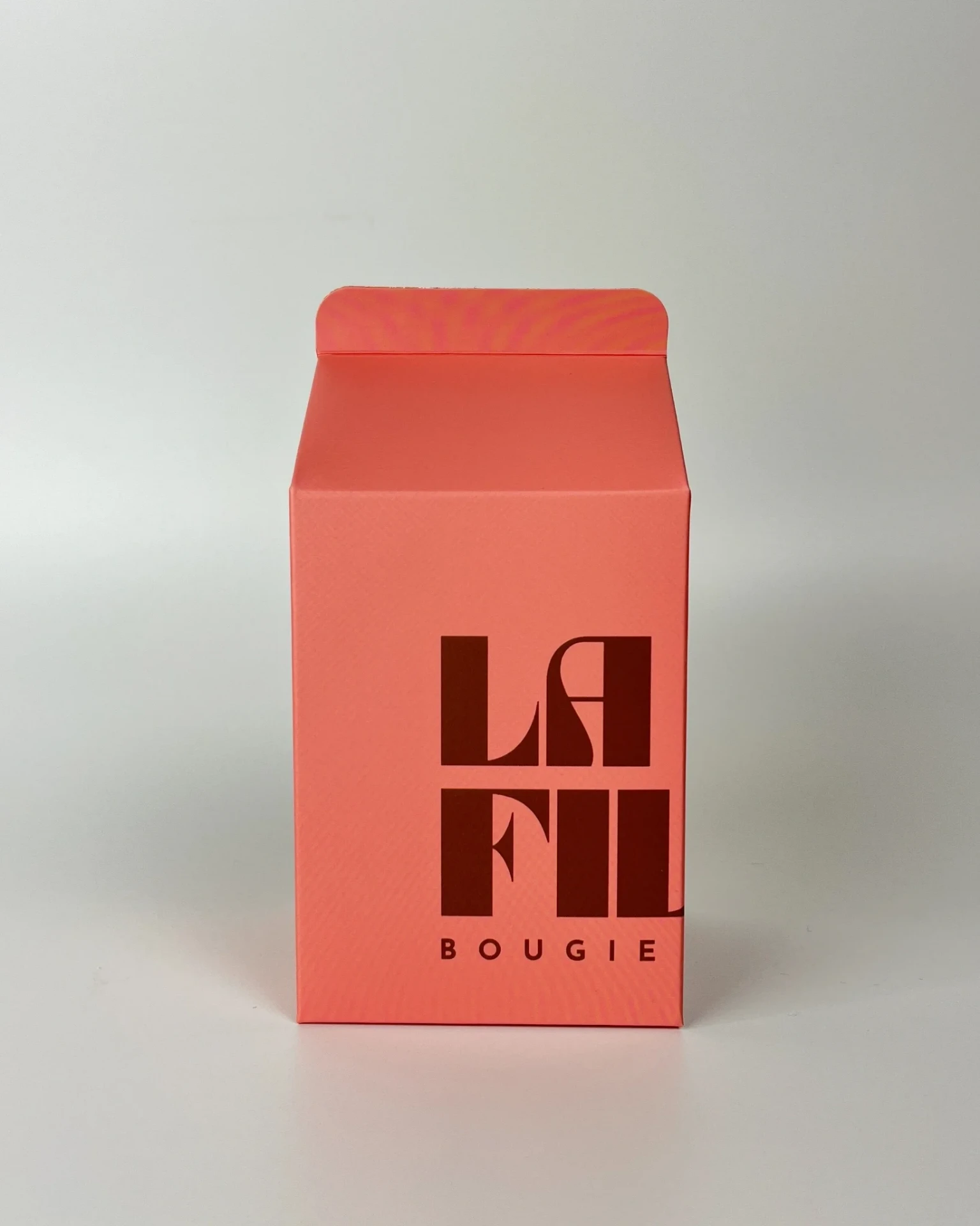 Front view of the rose and chocolate La Fille Milk Box packaging for the WOODS & TONKA scented candle.