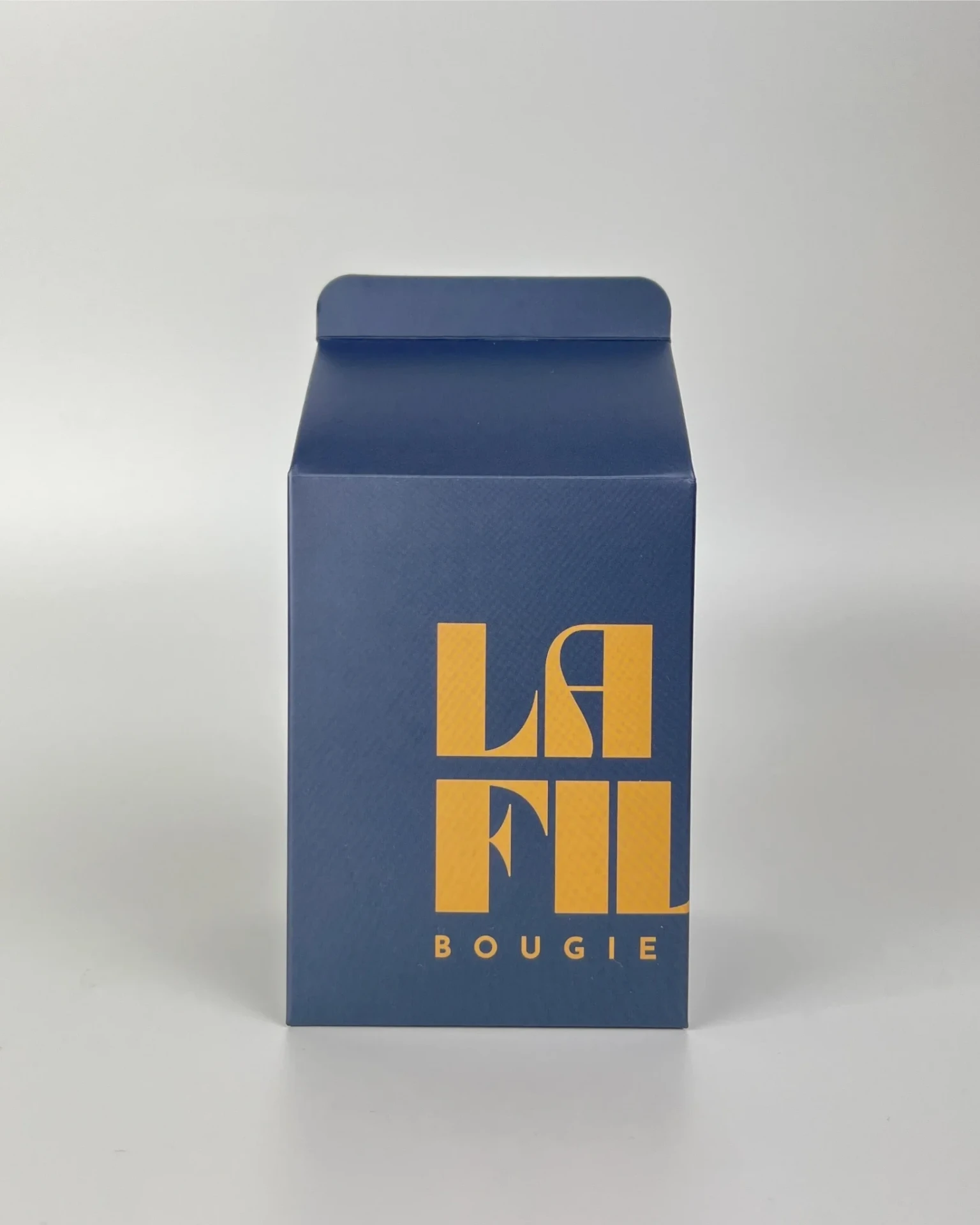 Front view of the navy blue and ochre La Fille Milk Box packaging for the BIBLIOTHÈQUE scented candle.