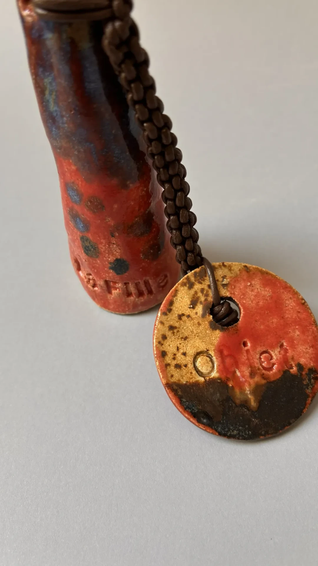 Détail des émaux Pacifik et Zinnoberrot, de la lanière en cuir tressé et du charm en céramique de Fire.