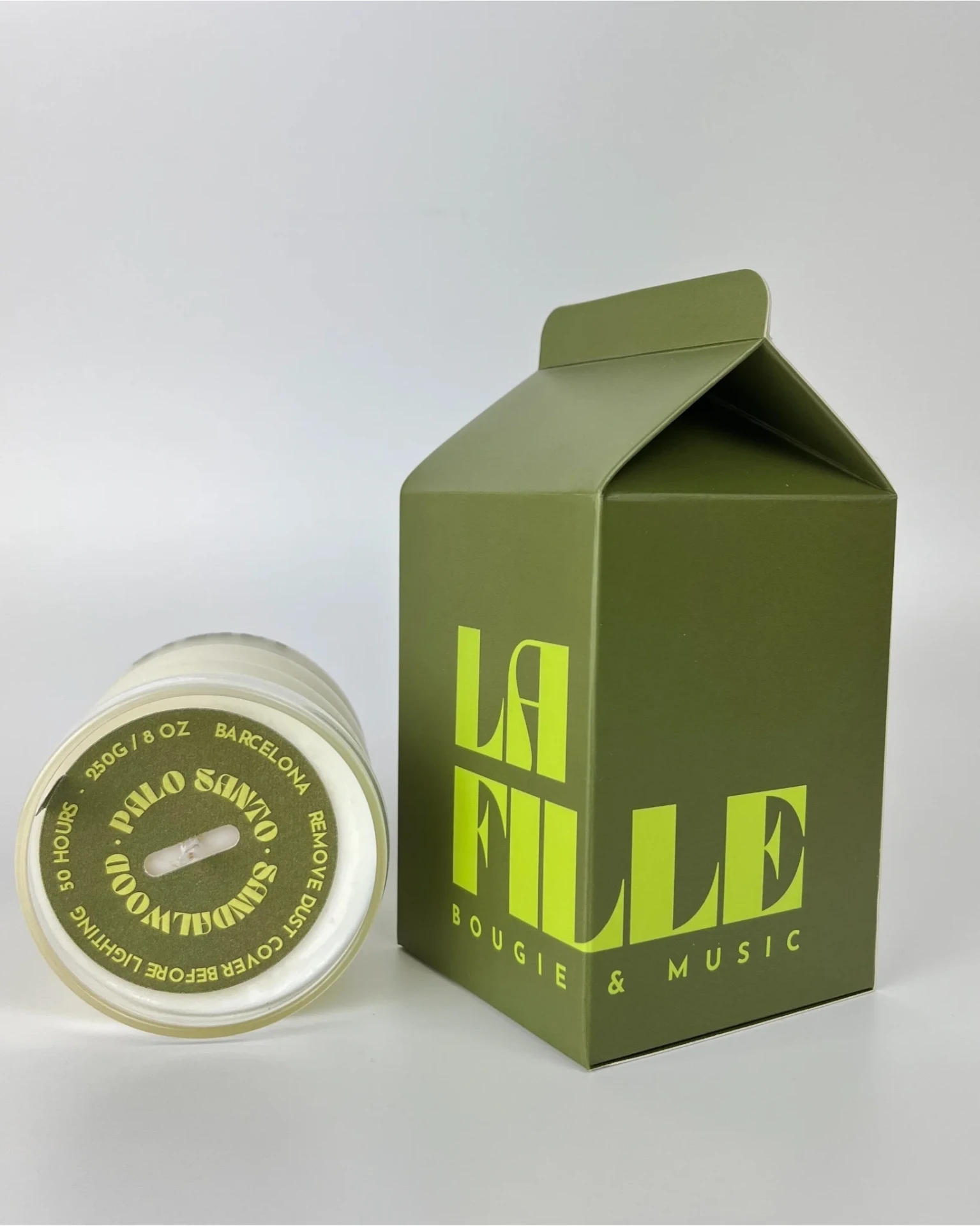 SANDALWOOD & PALO SANTO scented candle in a glass vessel beside its dark green and apple green La Fille Milk Box packaging.