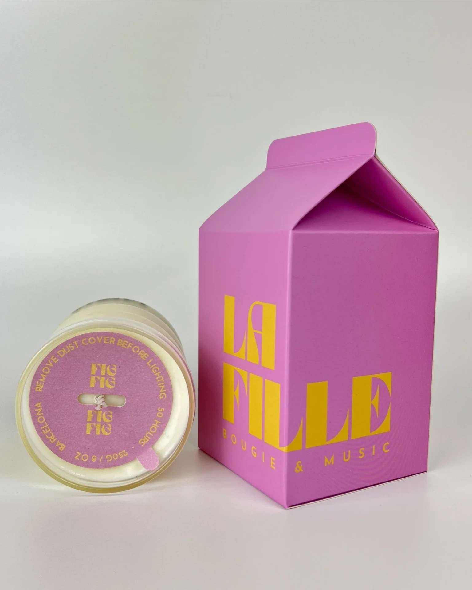 FIG scented candle in a glass vessel beside its lilac and vanilla La Fille Milk Box packaging.