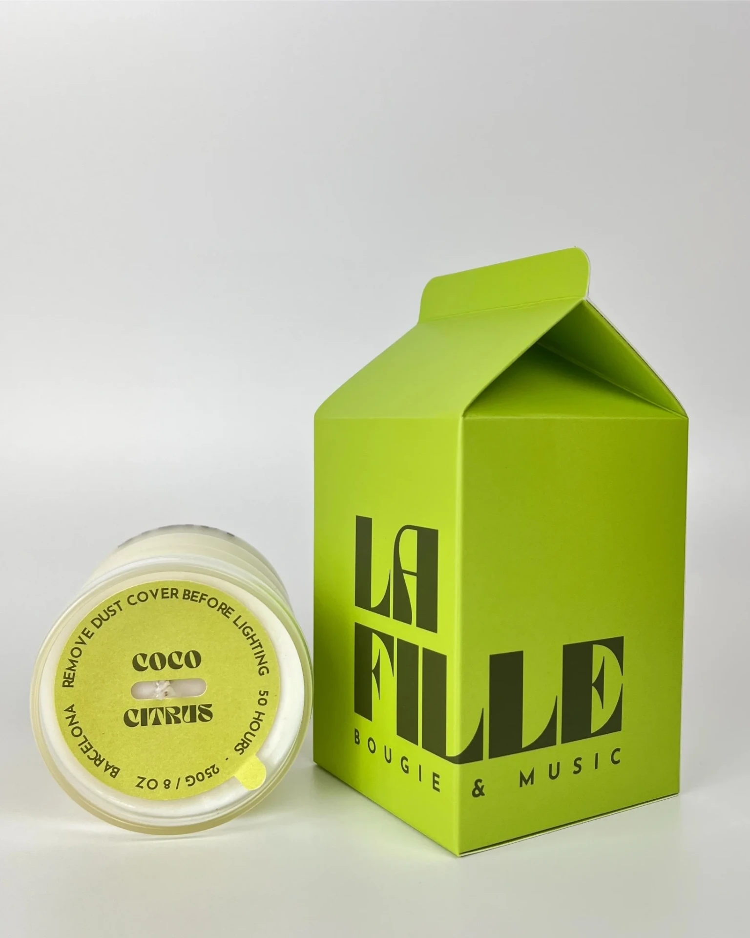 COCO & CITRUS scented candle in a glass vessel beside its apple green and dark green La Fille Milk Box packaging.