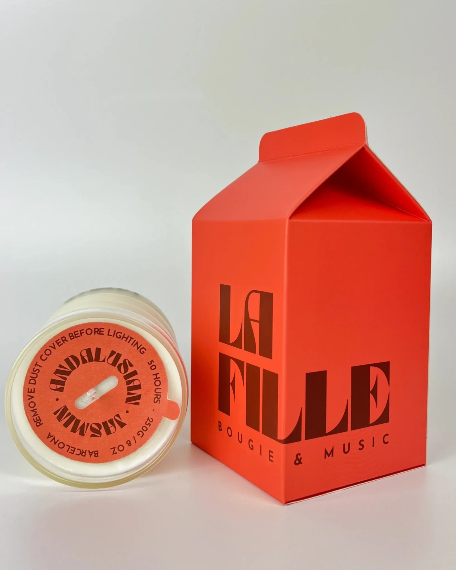 ANDALUSIAN JASMINE scented candle in a glass vessel beside its red and burgundy La Fille Milk Box packaging.
